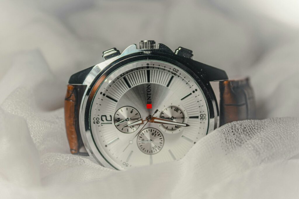 Close-up of a stylish analog watch with brown leather strap over soft fabric.